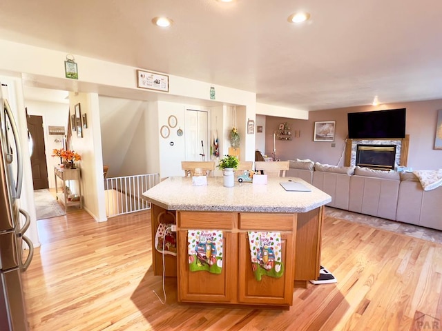 kitchen with brown cabinetry, freestanding refrigerator, open floor plan, an island with sink, and light wood-type flooring