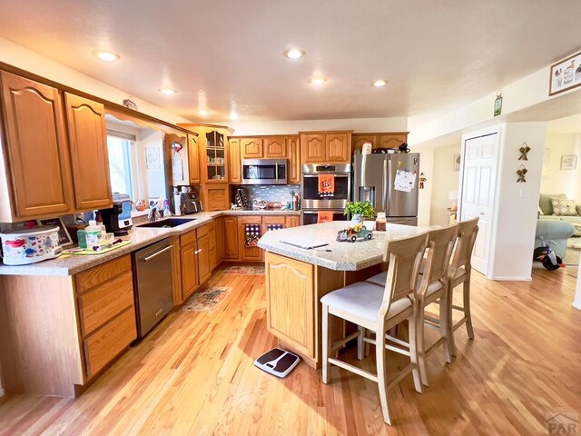 kitchen with a center island, a breakfast bar, appliances with stainless steel finishes, glass insert cabinets, and light wood-type flooring