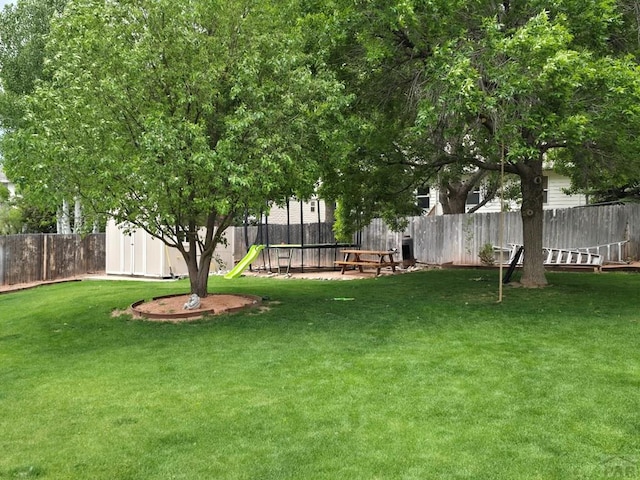 view of yard featuring a fenced backyard, an outbuilding, a trampoline, a storage unit, and a playground