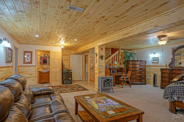 living area with visible vents, wainscoting, wood ceiling, a wood stove, and wood walls