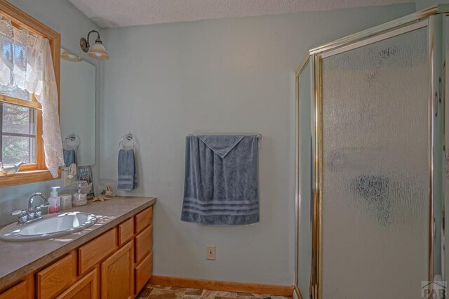 bathroom with a textured ceiling, a shower stall, vanity, and baseboards