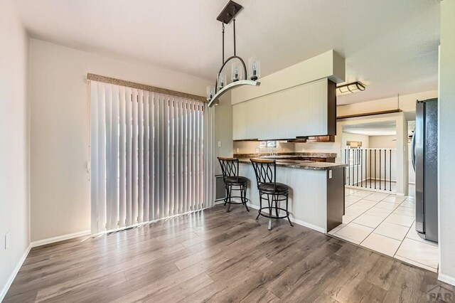 950 S Los Charros Dr, Pueblo West, CO 81007 - kitchen featuring freestanding refrigerator, dark countertops, light wood finished floors, a peninsula, and a breakfast bar