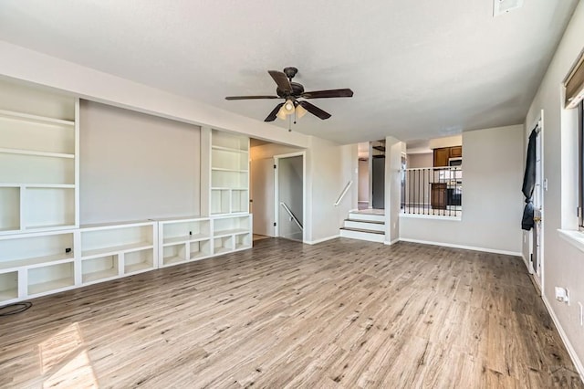 950 S Los Charros Dr, Pueblo West, CO 81007 - unfurnished living room featuring wood finished floors, a ceiling fan, built in shelves, and stairs