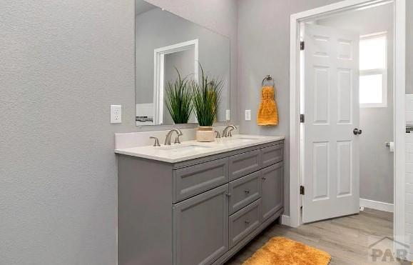 bathroom with double vanity, wood finished floors, baseboards, and a sink