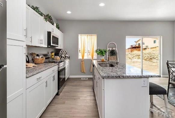 kitchen featuring an island with sink, a sink, stainless steel appliances, a breakfast bar area, and white cabinets