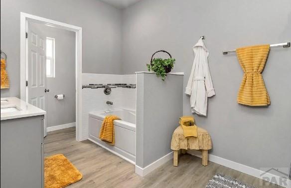 full bathroom with a bath, vanity, baseboards, and wood finished floors