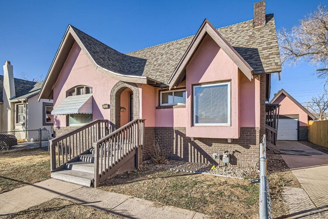 view of front of home featuring brick siding, roof with shingles, fence, and stucco siding