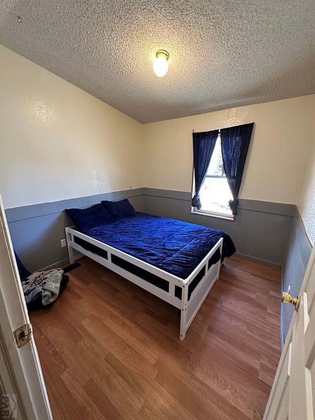 bedroom with a textured ceiling, wood finished floors, and wainscoting