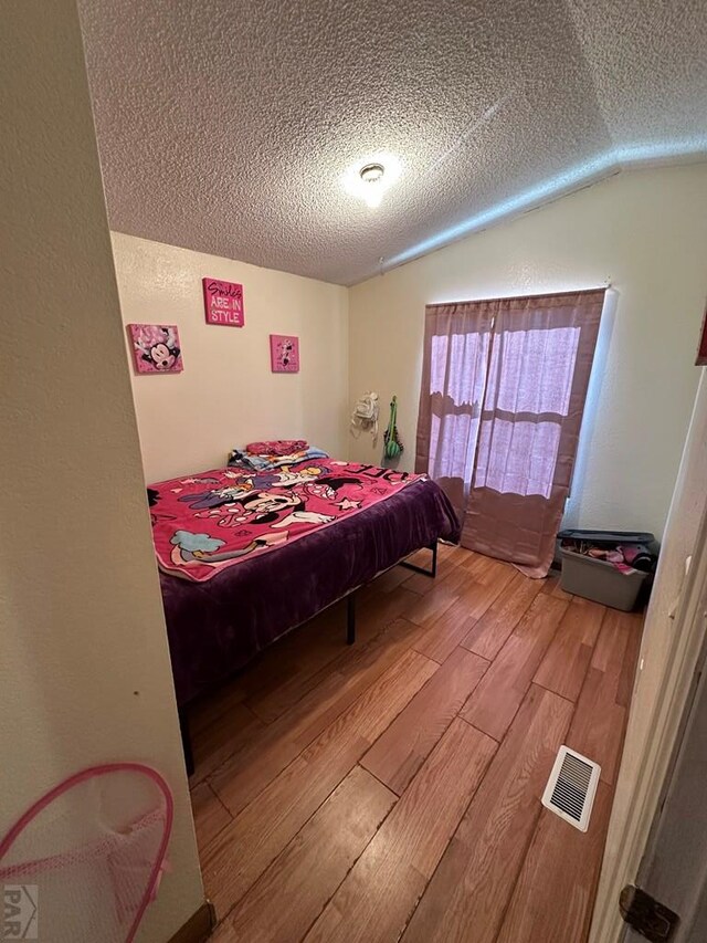 bedroom with vaulted ceiling, a textured ceiling, wood finished floors, and visible vents