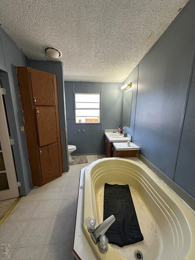 full bathroom with toilet, tile patterned floors, a textured ceiling, vanity, and a bath