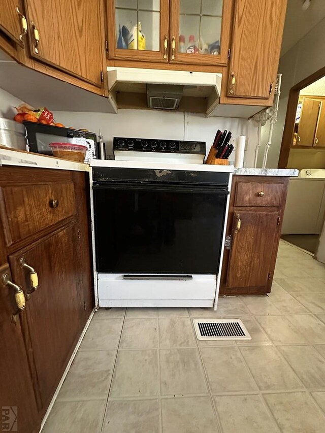 kitchen featuring light countertops, electric range, glass insert cabinets, brown cabinetry, and under cabinet range hood