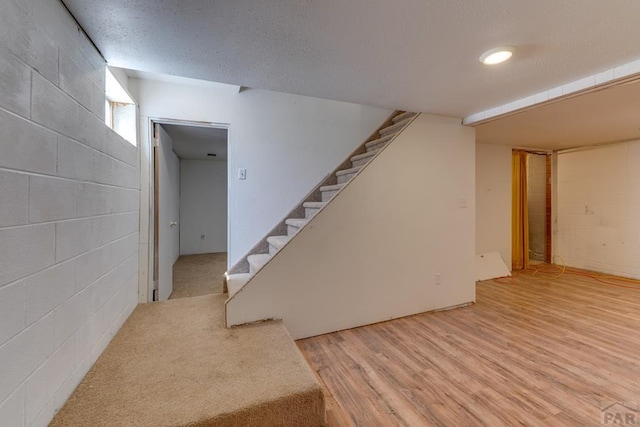 below grade area with concrete block wall, stairway, a textured ceiling, and wood finished floors