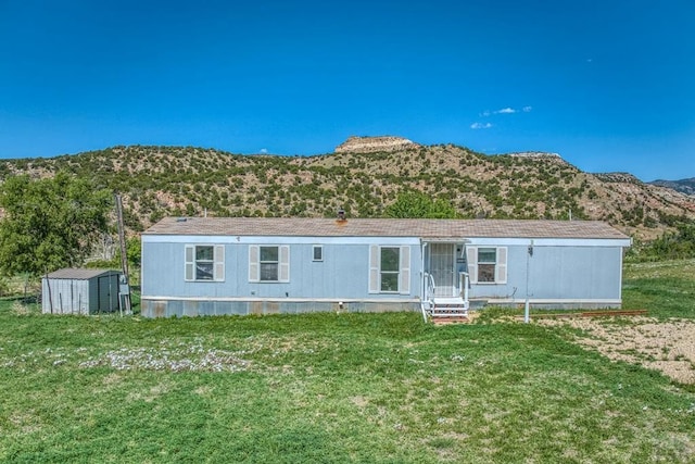 view of front facade with a front lawn, a storage unit, a mountain view, and an outbuilding