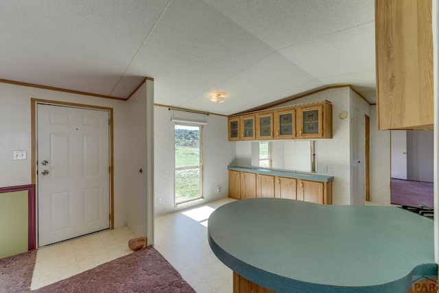 kitchen featuring glass insert cabinets, a peninsula, vaulted ceiling, a textured ceiling, and light floors