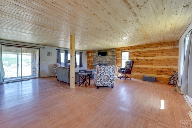 unfurnished living room with wooden ceiling, a fireplace, wooden walls, and light wood finished floors