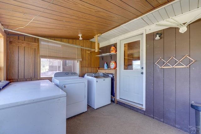 clothes washing area featuring laundry area, wooden ceiling, washer and dryer, carpet flooring, and wood walls