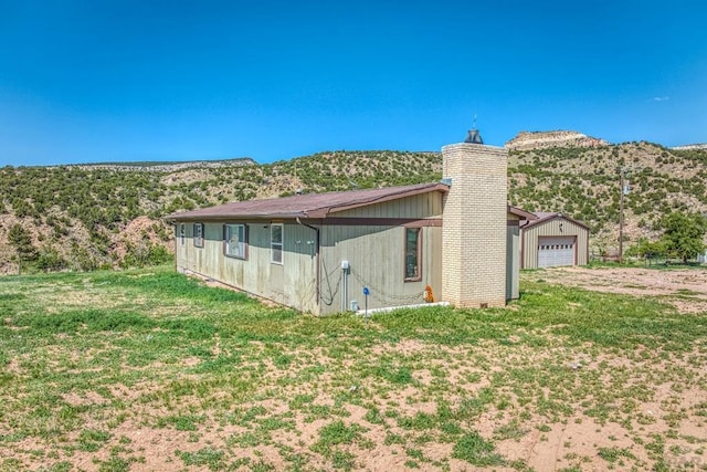 view of side of property featuring a garage, driveway, a chimney, and a lawn