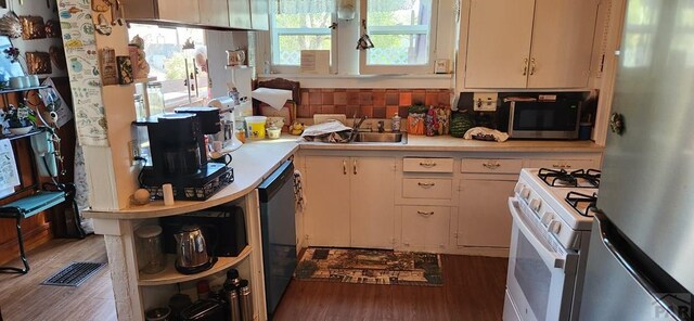 kitchen with white gas stove, wood finished floors, black dishwasher, light countertops, and freestanding refrigerator