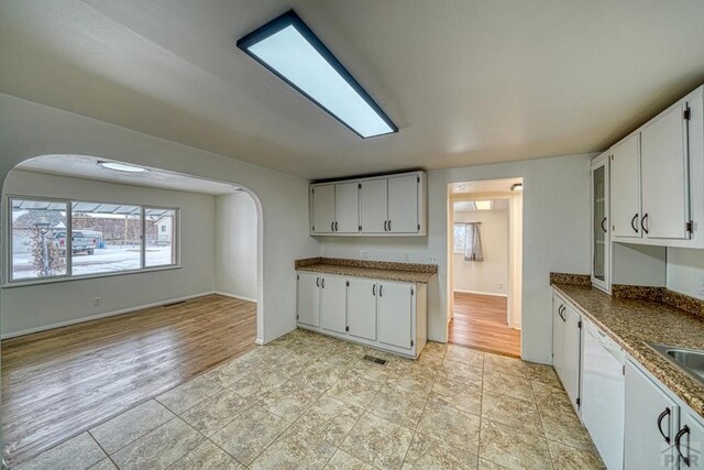 kitchen with arched walkways, light wood finished floors, white cabinets, a sink, and dishwasher