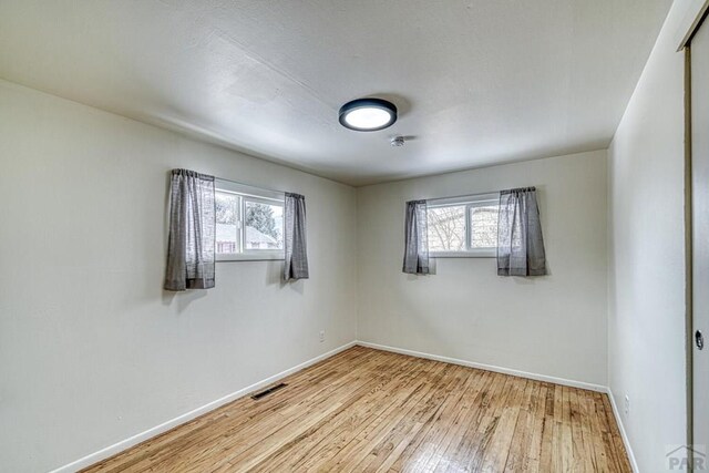 unfurnished room featuring a healthy amount of sunlight, baseboards, visible vents, and wood finished floors