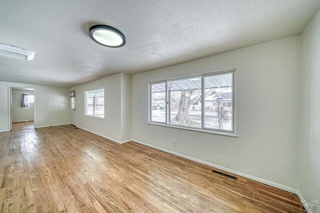 empty room featuring light wood-type flooring, baseboards, visible vents, and a textured ceiling