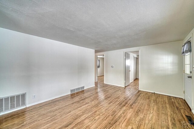 spare room with baseboards, visible vents, a textured ceiling, and light wood finished floors