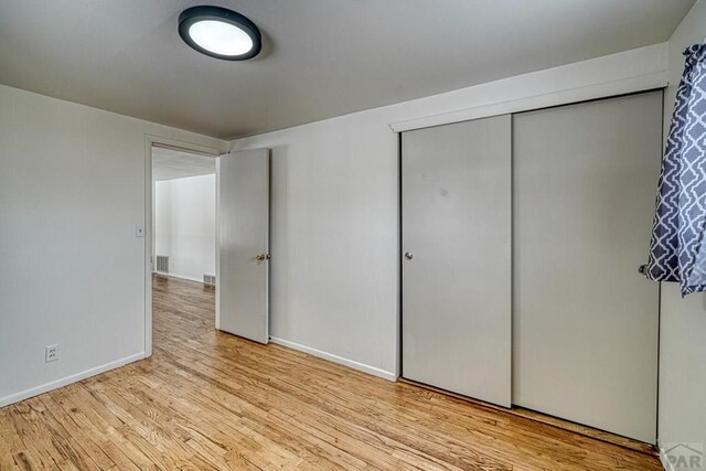 unfurnished bedroom featuring light wood-style floors, visible vents, baseboards, and a closet