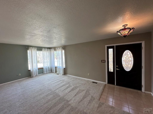 foyer entrance with visible vents, light carpet, light tile patterned flooring, a textured ceiling, and baseboards