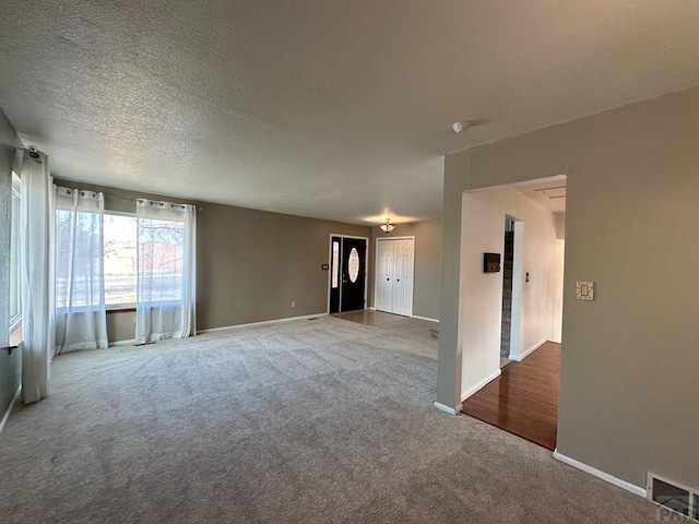 unfurnished living room featuring a textured ceiling, carpet, visible vents, and baseboards