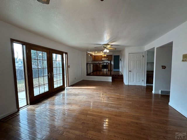 unfurnished living room featuring dark wood-style floors, french doors, visible vents, a textured ceiling, and baseboards