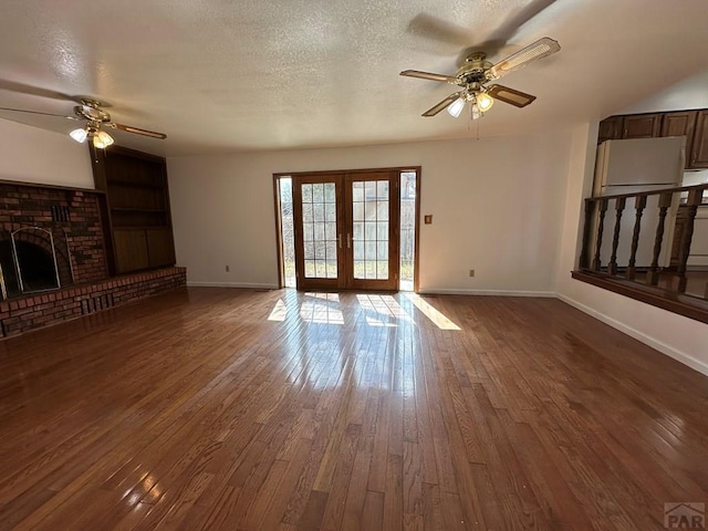 unfurnished living room featuring a textured ceiling, baseboards, french doors, a brick fireplace, and dark wood-style floors