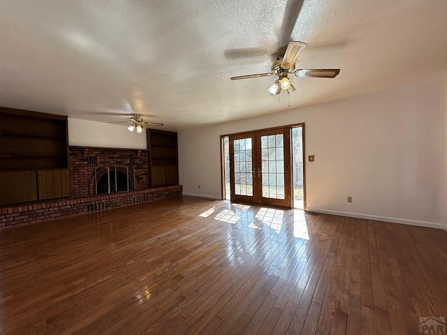 unfurnished living room with french doors, a fireplace, dark wood finished floors, ceiling fan, and a textured ceiling