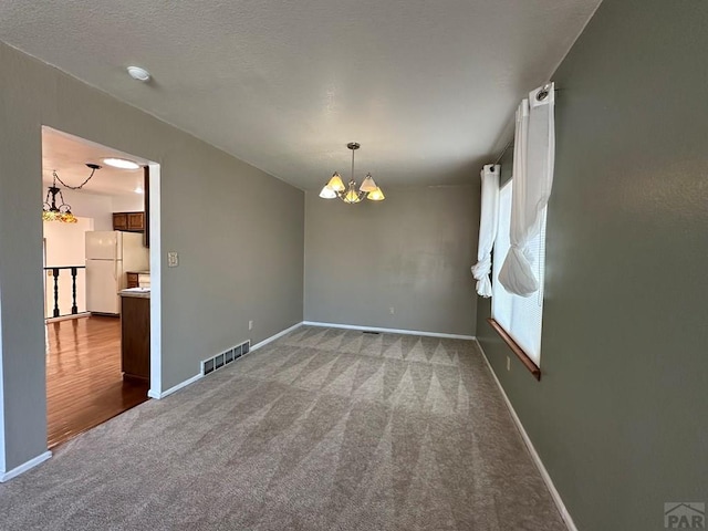 unfurnished room featuring baseboards, carpet flooring, visible vents, and a notable chandelier