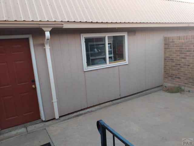 doorway to property featuring metal roof, a patio, and brick siding