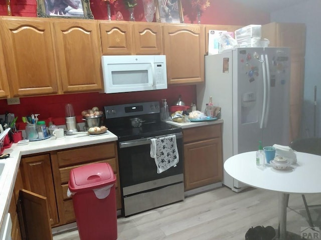 kitchen with brown cabinets, white appliances, light countertops, and light wood finished floors