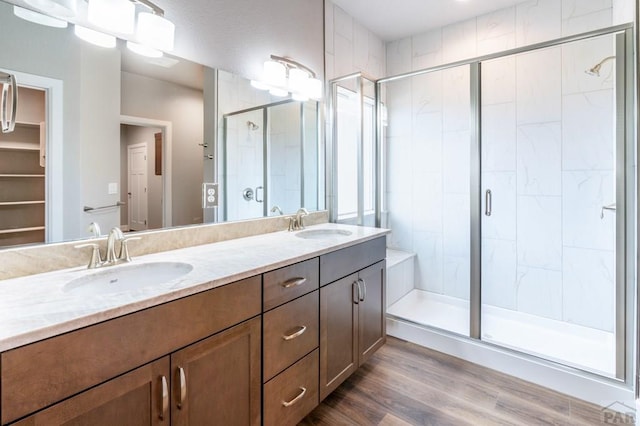 bathroom featuring a shower stall, wood finished floors, double vanity, and a sink