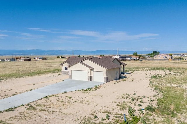 view of home's exterior with a mountain view, an attached garage, stone siding, stucco siding, and driveway