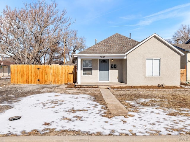 bungalow-style home with roof with shingles, fence, and stucco siding