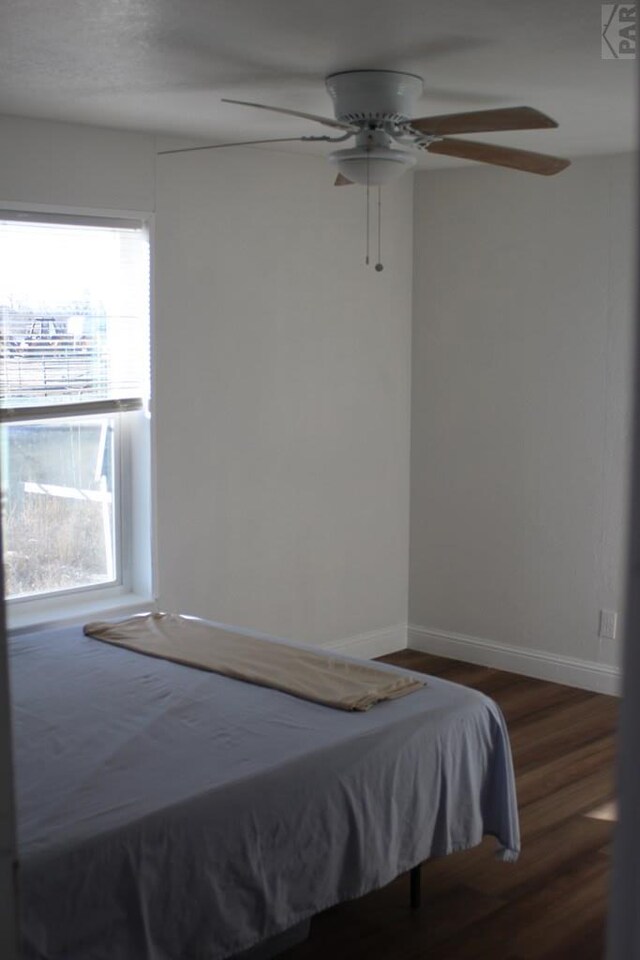 unfurnished bedroom with ceiling fan, baseboards, and dark wood-type flooring