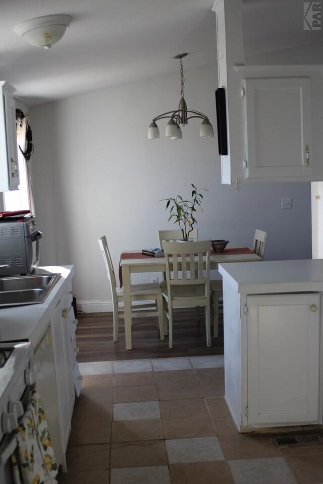 kitchen featuring decorative light fixtures, an inviting chandelier, light countertops, white cabinetry, and a sink