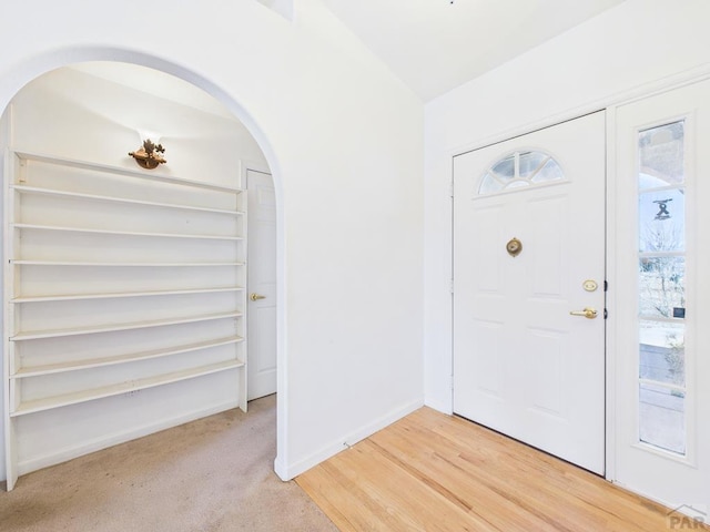 entrance foyer with arched walkways, light colored carpet, and baseboards