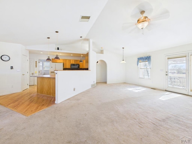 unfurnished living room featuring light carpet, arched walkways, visible vents, and a ceiling fan