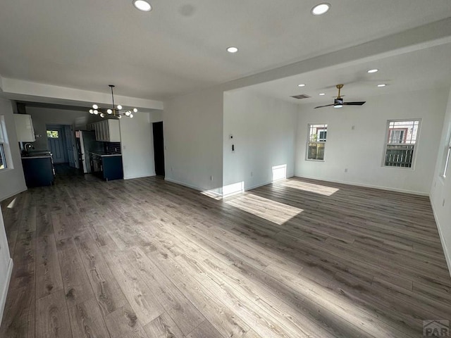 unfurnished living room featuring recessed lighting, ceiling fan with notable chandelier, dark wood-type flooring, visible vents, and baseboards