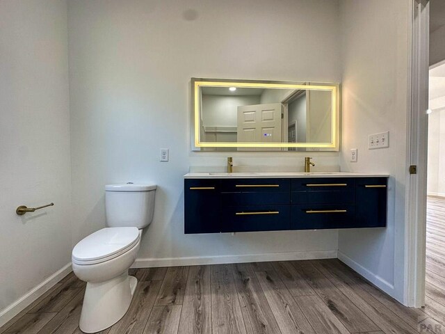 bathroom featuring toilet, wood finished floors, a sink, baseboards, and double vanity