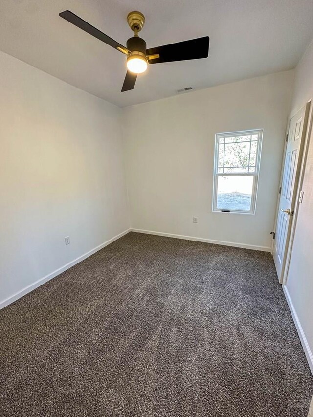 spare room featuring baseboards, visible vents, dark carpet, and a ceiling fan