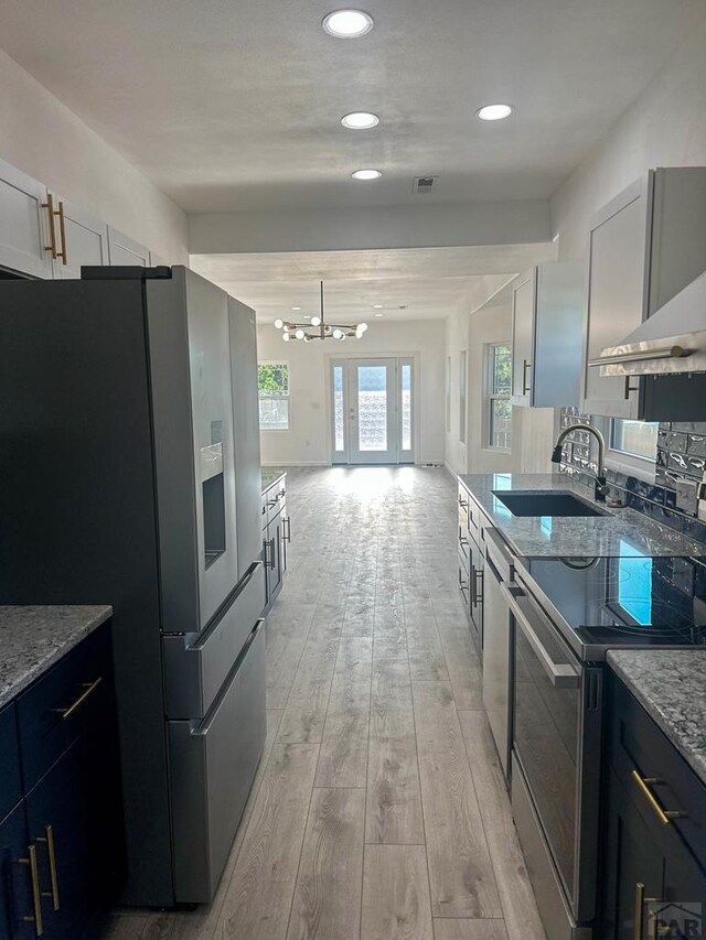 kitchen featuring appliances with stainless steel finishes, open floor plan, light stone countertops, light wood-type flooring, and a sink