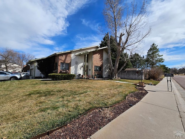 mid-century home with brick siding, an attached garage, a front lawn, and fence