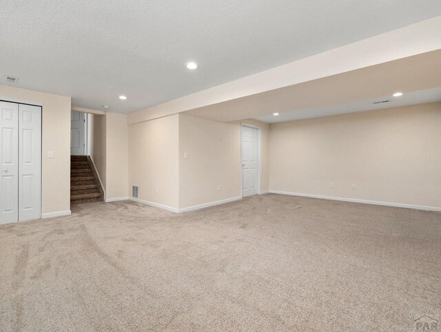 finished basement with baseboards, stairs, a textured ceiling, carpet flooring, and recessed lighting