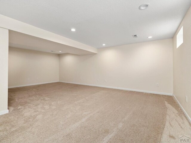 finished basement featuring light carpet, visible vents, baseboards, a textured ceiling, and recessed lighting