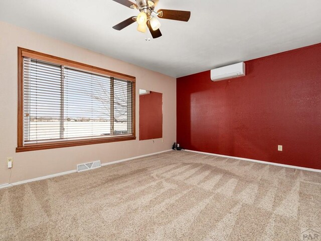 carpeted spare room with baseboards, visible vents, ceiling fan, and an AC wall unit